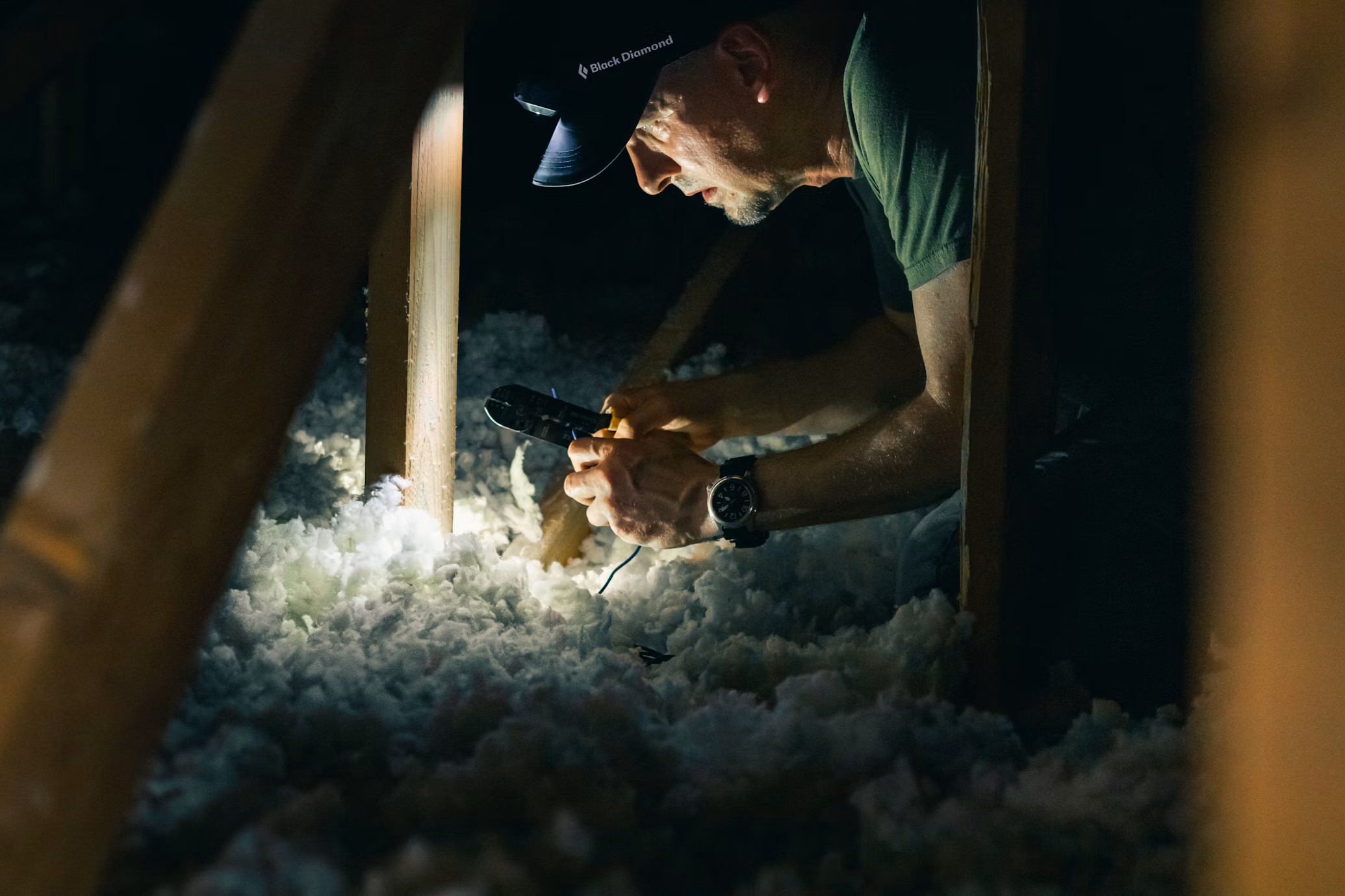 A person is in an attic space, installing sustainable insulation. The insulation is made of natural fibers or recycled materials.