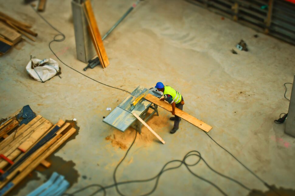 A construction worker using an electric saw to cut a large piece of plywood.