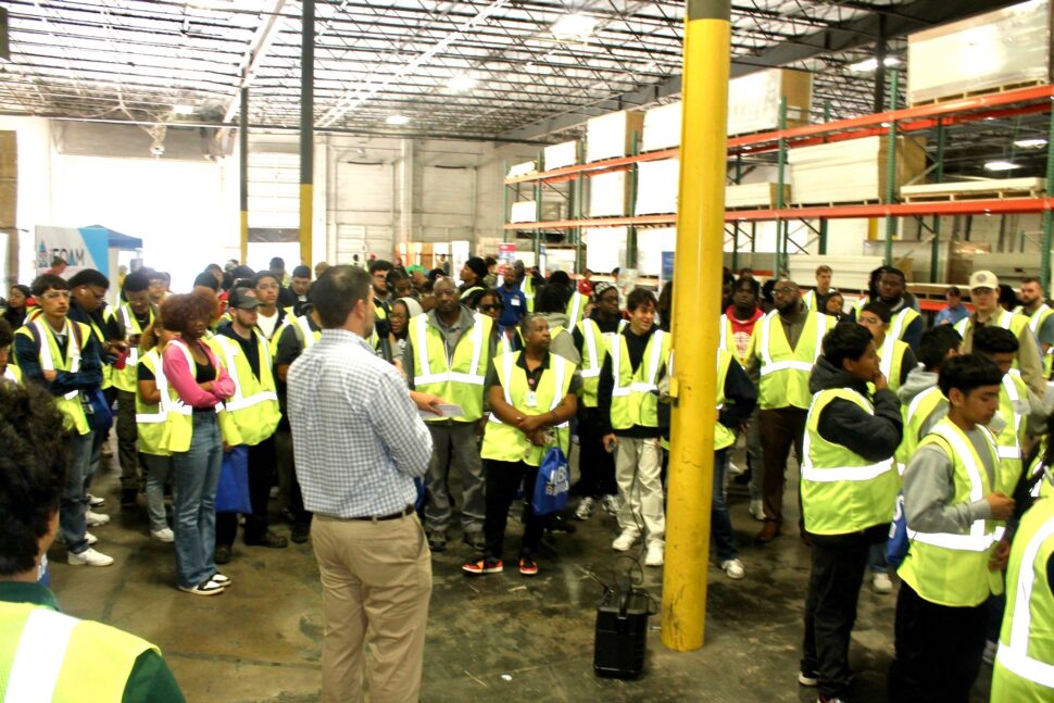 The picture depicts people in a warehouse with yellow construction vests on.
