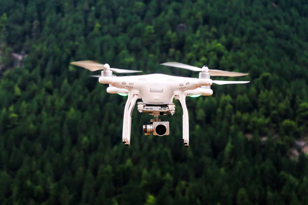 A white drone is flying above trees.