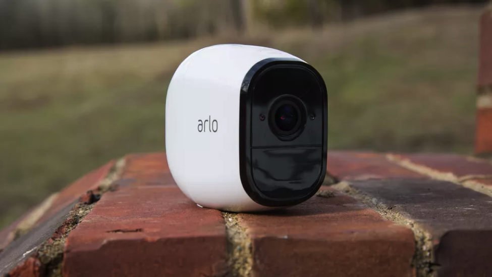 Arlo device. it is placed on a brick stair and the device is white and the area around the camera is black