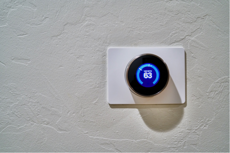 Nest thermostat on the wall of a home. The thermostat is digital with blue and white writing.